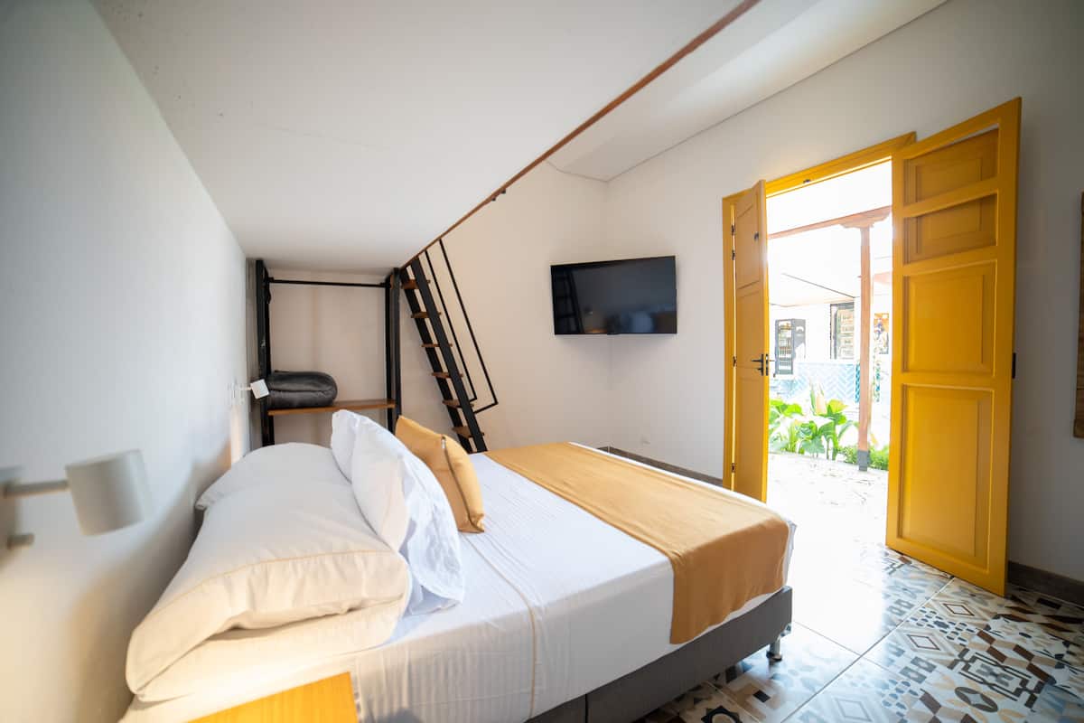 A bedroom with a bed, a TV mounted on the wall, and a door leading outside.
