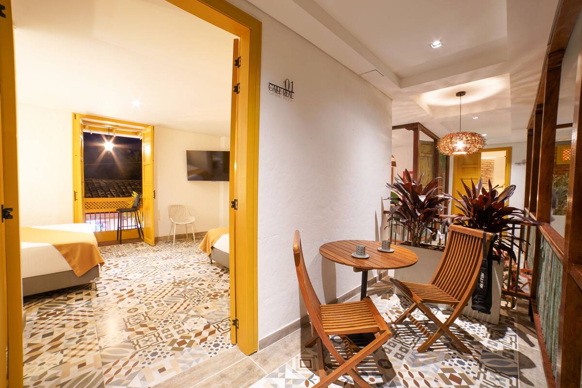 A hotel room with a bed, a desk, and a chair. There is a dining area with a table and chairs.
