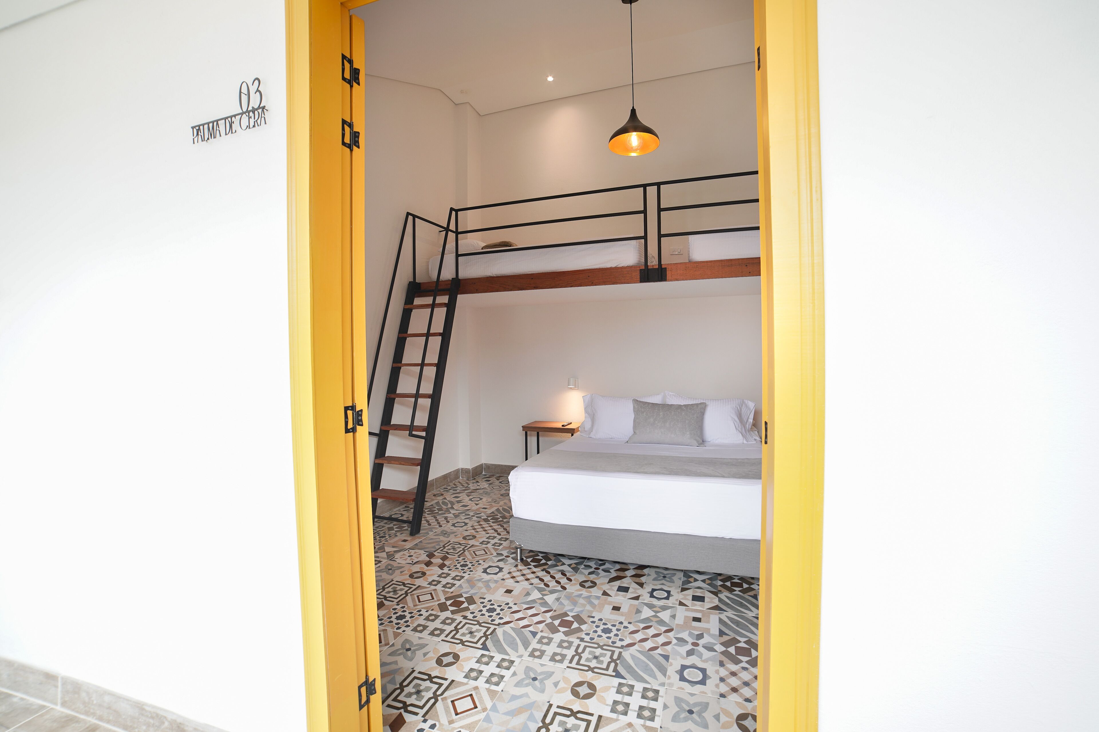 A room with a bunk bed, a ladder, a bedside table, and a patterned floor.