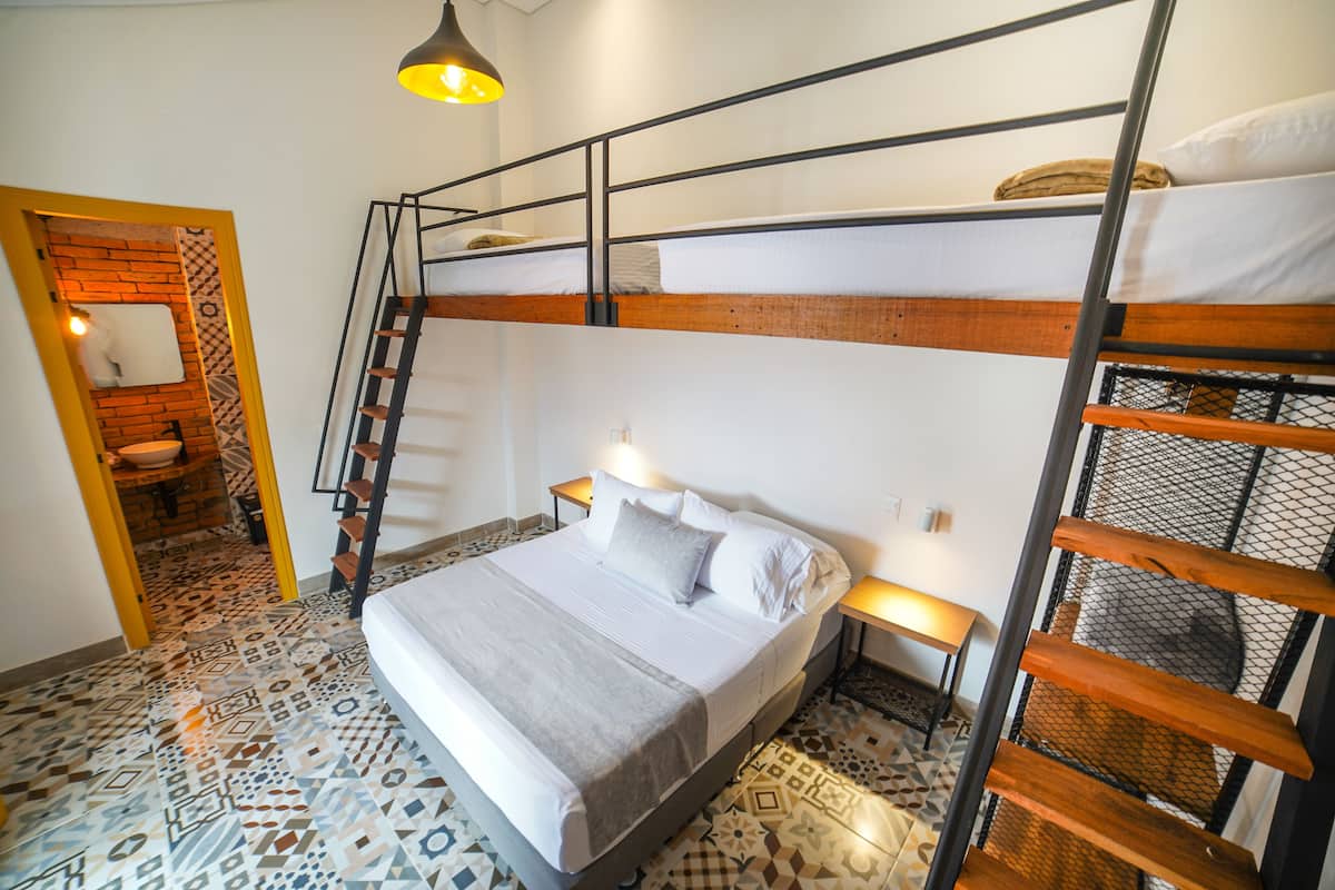 A bunk bed room with a patterned floor, a small bathroom with a brick wall, and a staircase.