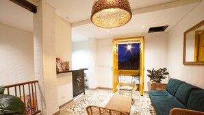 Un espacio de sala moderno con un sofá, sillas de mimbre, piso estampado y una lámpara decorativa en el techo.