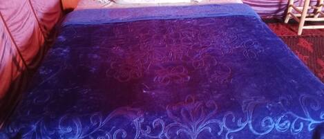 A bed with a blue and purple bedspread, a white pillow, and a wooden chair in the background.