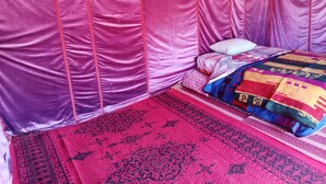 A room with a bed covered in a patterned blanket, a red and black rug, and a pink canopy. - BIVOUAC CÔTE-IRIKI (Allougoum)