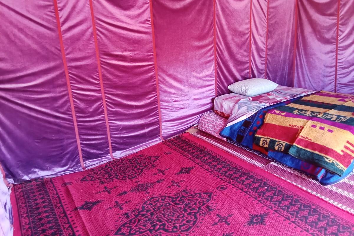 Una habitación con una cama cubierta por una manta estampada, un tapete rojo y negro, y un dosel rosa.