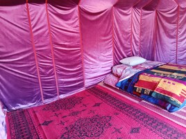 Una habitación con una cama cubierta por una manta estampada, un tapete rojo y negro, y un dosel rosa.