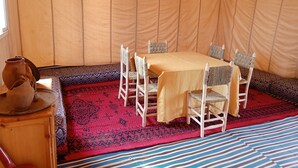 A tent with a dining table and chairs, a patterned rug, and a wooden table with a pot. - BIVOUAC CÔTE-IRIKI (Allougoum)