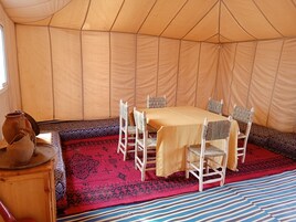 Una carpa con una mesa de comedor y sillas, un tapete estampado y una mesa de madera con una olla.