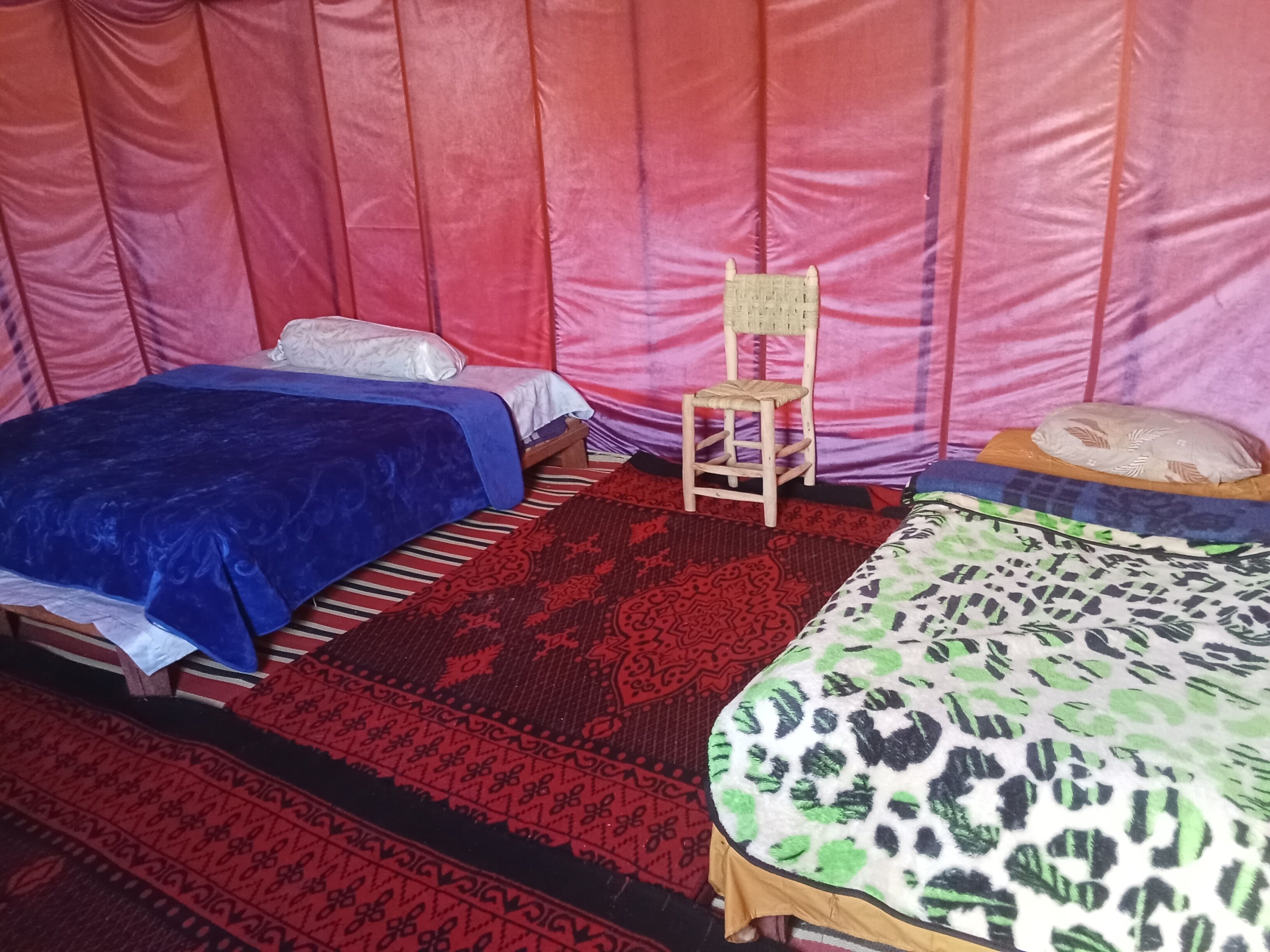 A room with two beds, a small wooden chair, and patterned rugs.