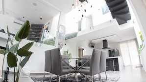 Un interior moderno con zona de comedor que incluye una mesa de vidrio y sillas grises, una escalera y una cocina.