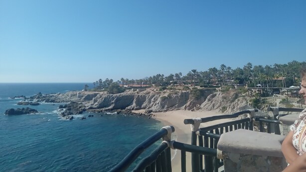 A coastal view with a clear sky, rocky coastline, and a beach with palm trees. - Hacienda La Ballena  (Cabo San Lucas)