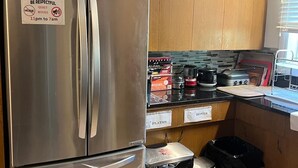 Una cocina con un refrigerador de acero inoxidable, gabinetes de madera, una encimera con electrodomésticos de cocina y contenedores de almacenamiento etiquetados.