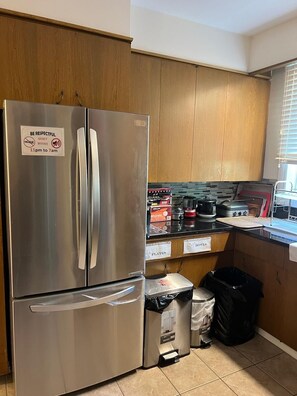 A kitchen with a stainless steel refrigerator, wooden cabinets, a countertop with cooking appliances, and labeled storage bins.