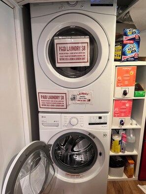 A front-loading washing machine with a sign indicating a paid laundry service for $8, including detergent, fabric softener, and dryer sheet.