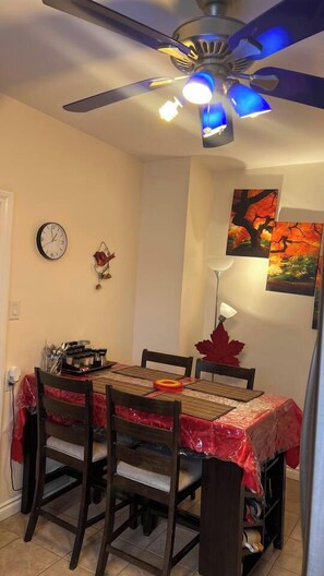 A dining area with a table set for four, a ceiling fan, wall-mounted clock, and artwork. - #1(5* Room PRIME LOCALITy WPG Jets {Nr Polo Park} (Winnipeg)