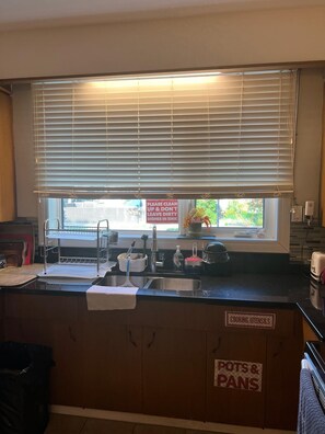 A kitchen with a sink, a window with blinds, and a sign indicating where to place dishes and cooking utensils.