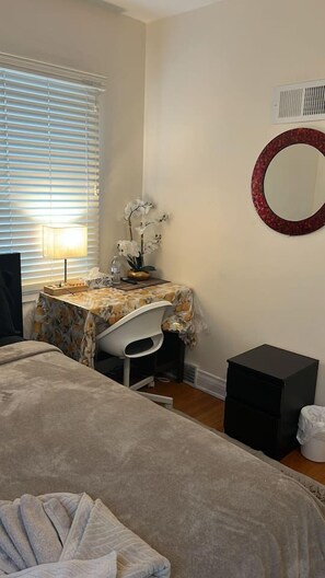 Une chambre à coucher comprenant un lit, un bureau avec une chaise, une petite table avec une lampe, un miroir et un radiateur.