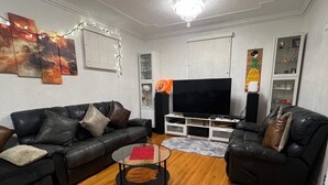 A living room with two black leather sofas, a glass coffee table, a flat-screen TV, and a white cabinet.