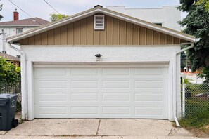Un garage avec une porte blanche, un toit marron et une petite grille d’aération.