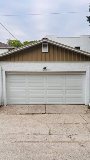 Un garage avec une porte blanche, un pignon en bois et une petite grille d’aération.