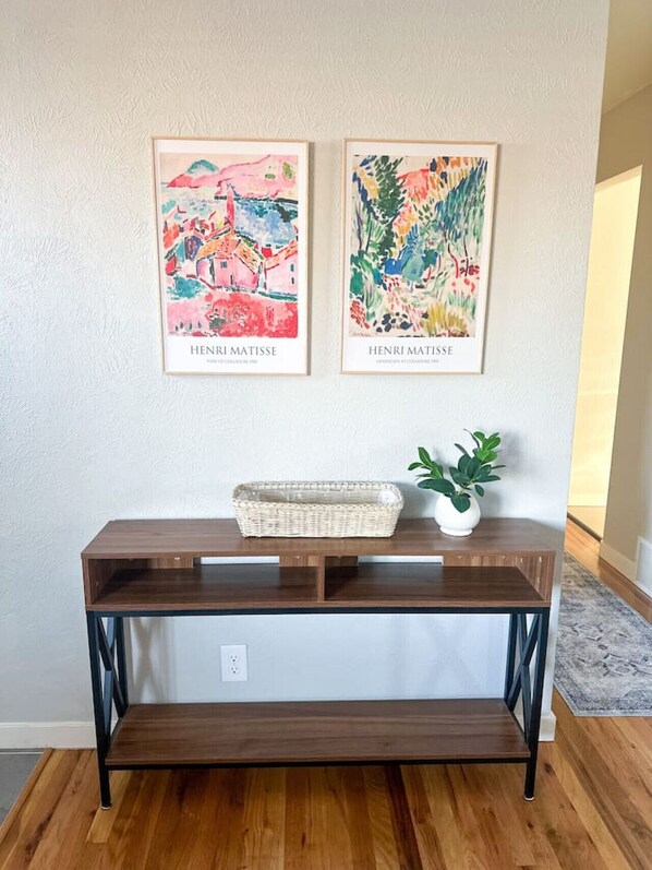 A wooden console table with two framed artworks by Henri Matisse, a woven basket, and a potted plant. - The Thornton Retreat – Modern & Cozy Stay (Thornton)