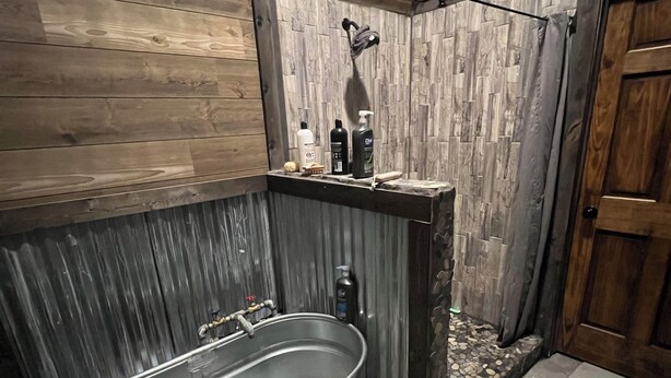 A rustic bathroom with a large metal bathtub labeled 'TARTER', a wooden shower enclosure, and a wooden door.