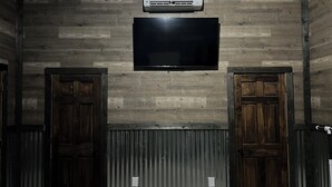 A room with a flat-screen TV mounted on a wooden wall, flanked by two wooden doors and a radiator below.