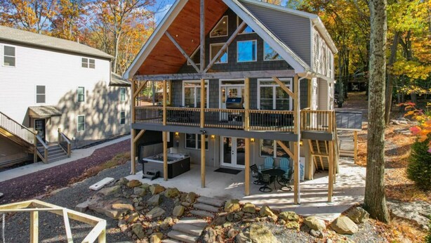 Una cabaña de varios pisos con terraza, un jacuzzi y una zona de estar exterior cubierta.