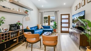 Un soggiorno moderno con un divano blu, due poltrone arancioni, una macchina del caffè e un televisore su un mobile in legno.