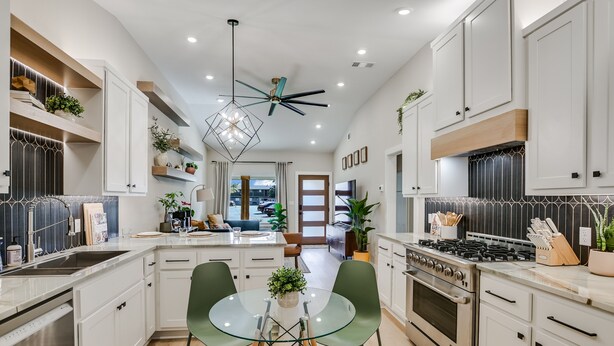 Una cucina moderna con mobili bianchi, un'isola centrale con piano in vetro e una ventola a soffitto.