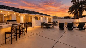 An outdoor patio with a bar area, seating, and a view of the sunset. - Pacifica Sur by Avantstay Pool, Hot Tub, Gazebo (Indio)