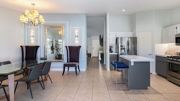 A modern kitchen with a built-in oven, a dining area with a glass table and chairs, and a hallway leading to a living space. - Pacifica Sur by Avantstay Pool, Hot Tub, Gazebo (Indio)