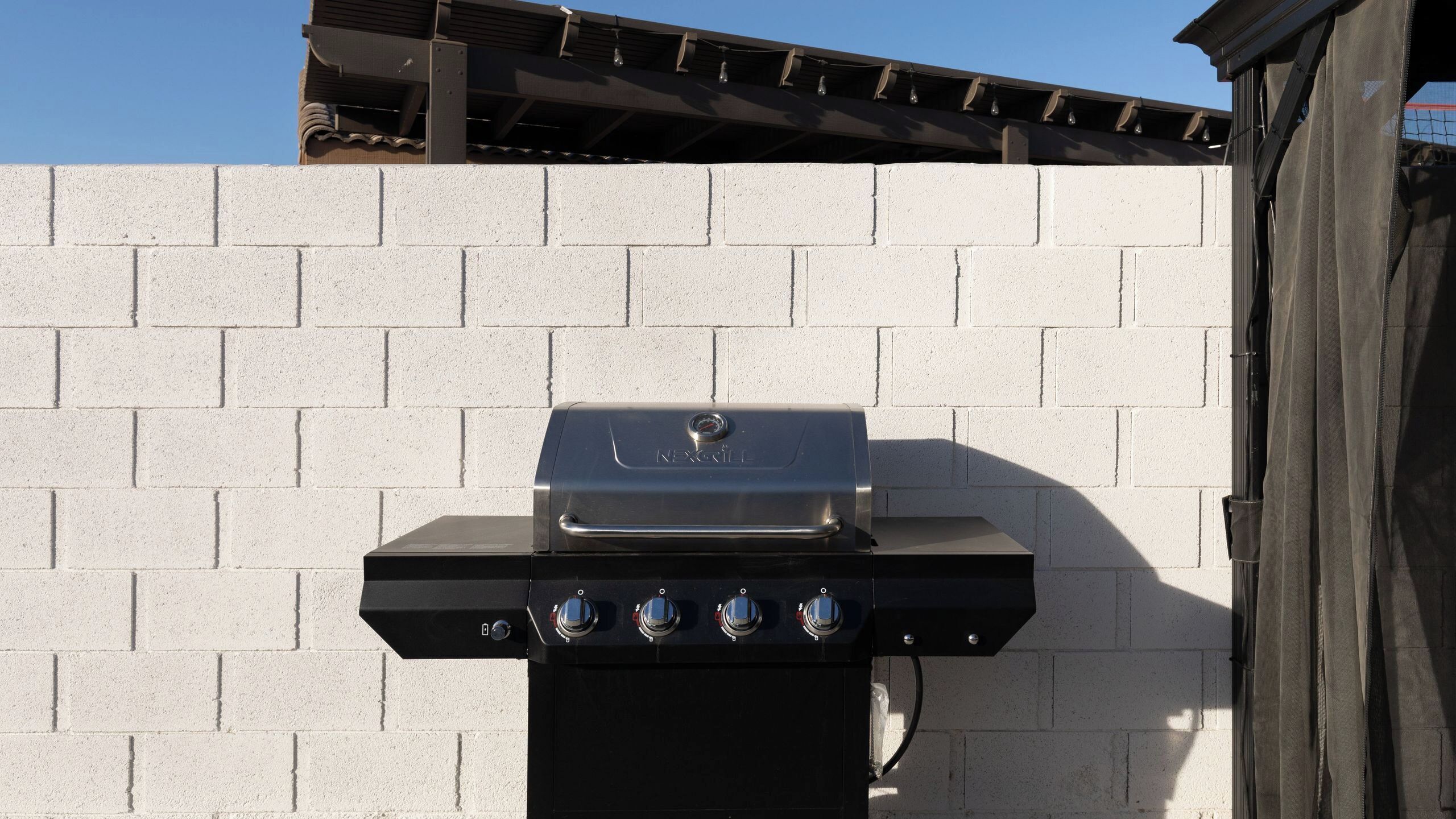 Una parrilla NRG Elite con cuatro perillas de control, sobre un muro de ladrillo blanco.