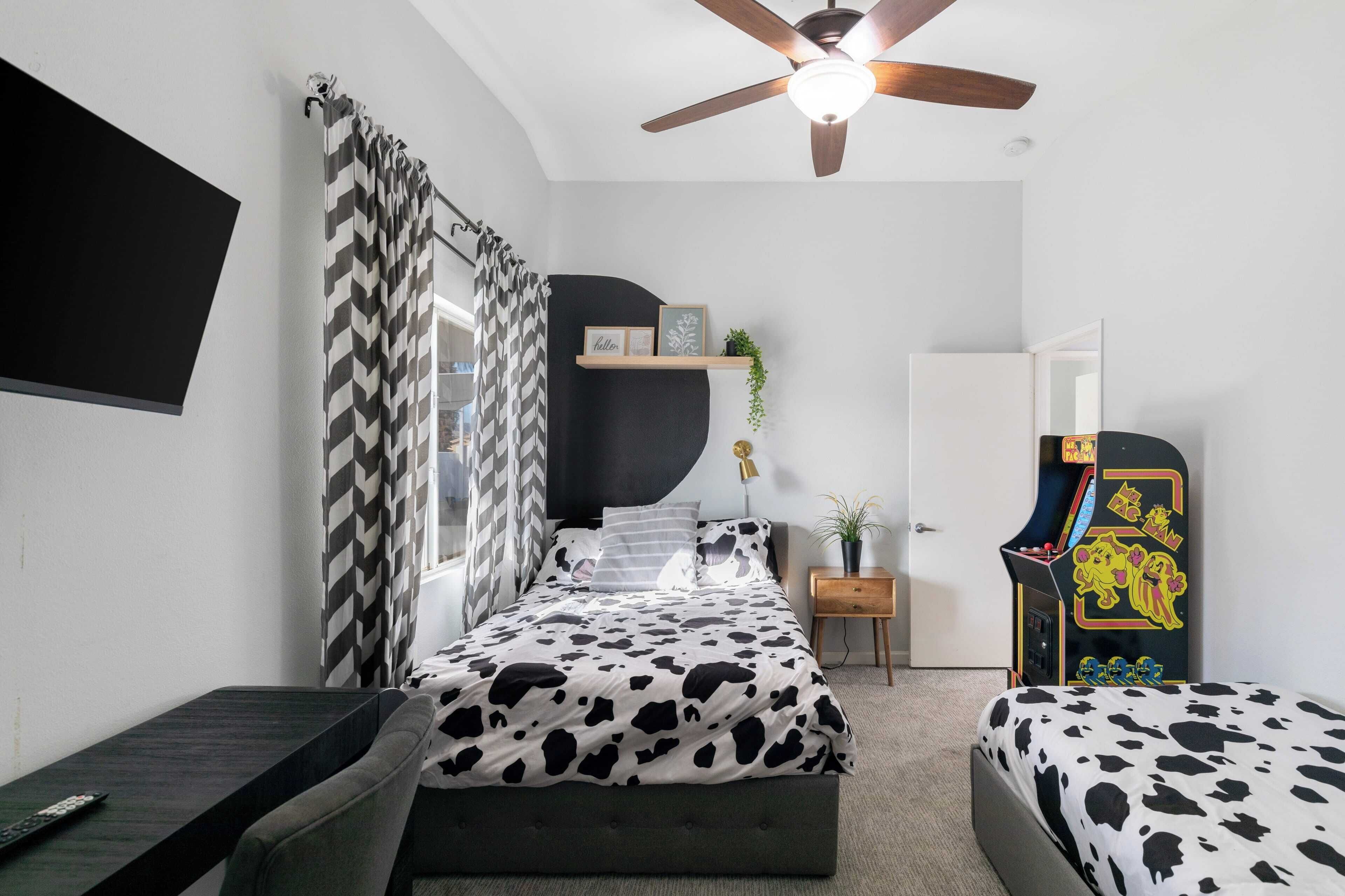 A bedroom with a bed, a desk, a ceiling fan, a TV, and a gaming console.