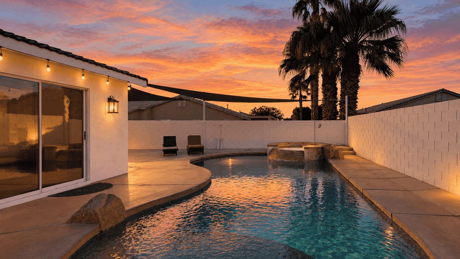A swimming pool with a curved design, surrounded by a white wall and palm trees.