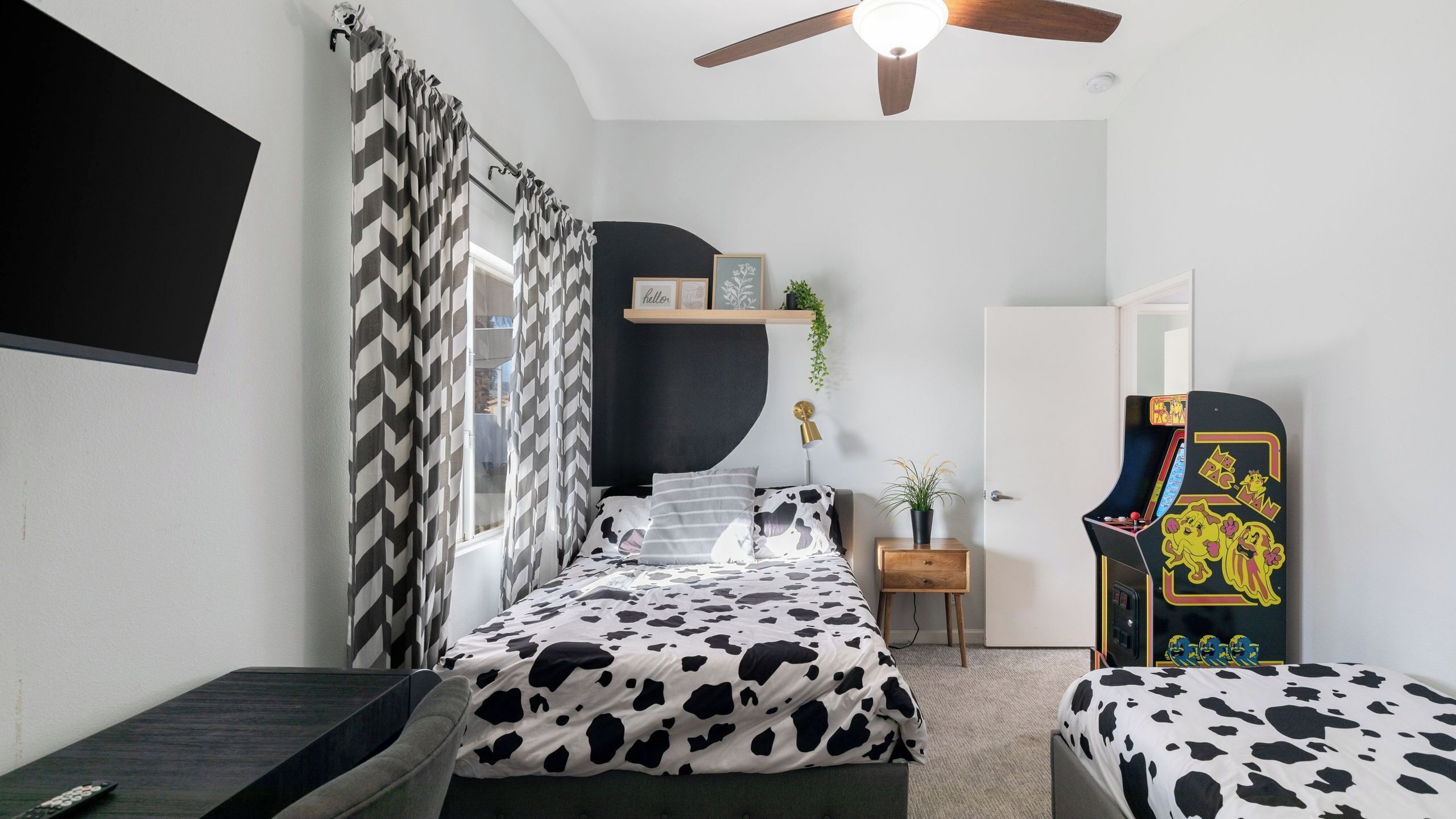 Une chambre à coucher comprenant un lit, un bureau, une chaise, un ventilateur de plafond et une console de jeux.