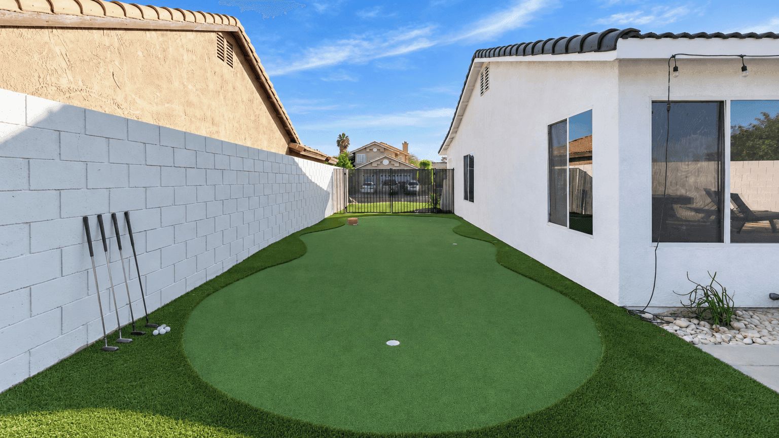 A backyard with artificial green turf, a white brick wall, and a small fenced area.