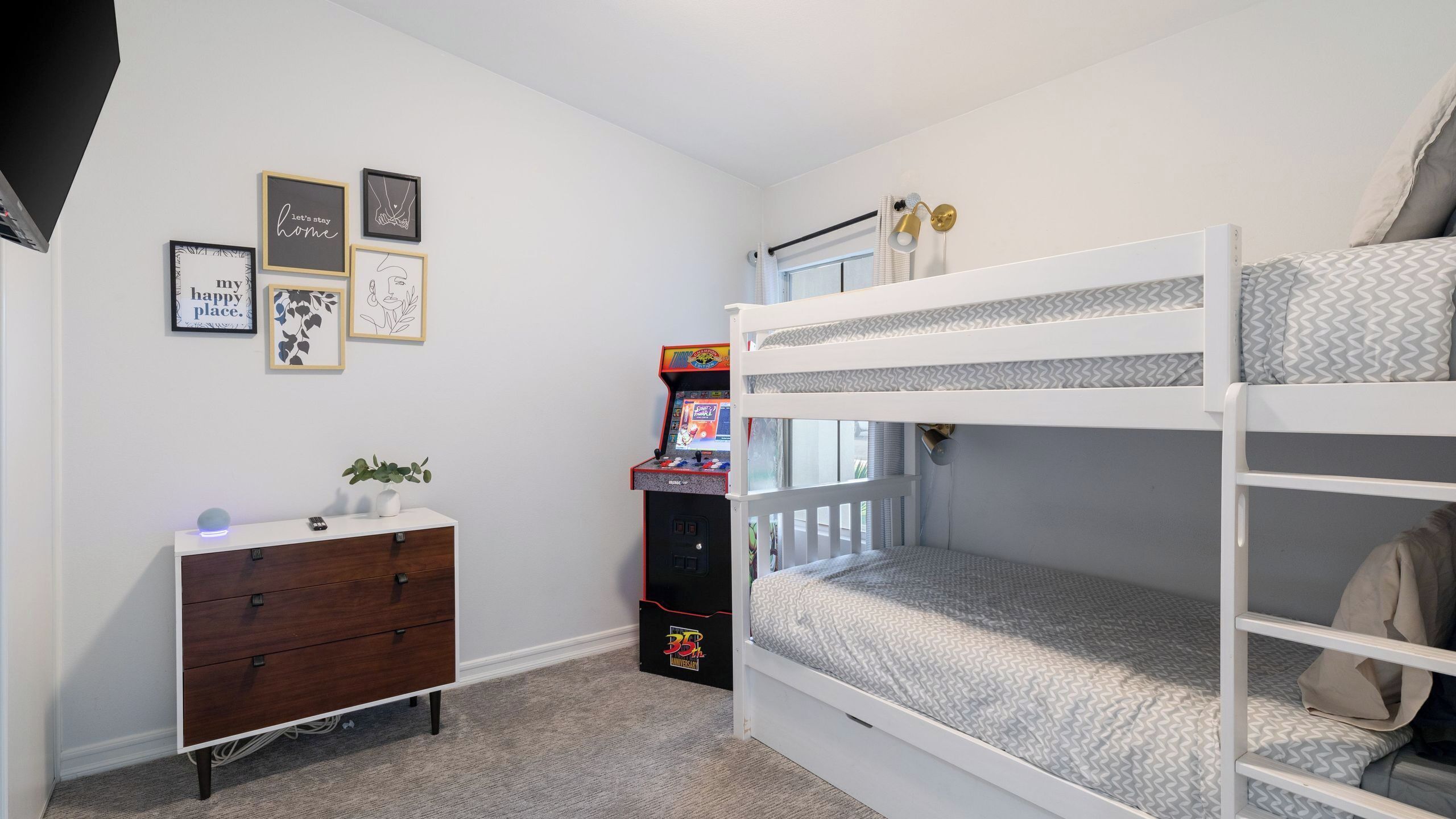 A bunk bed room with a dresser, a small arcade machine, and wall art.