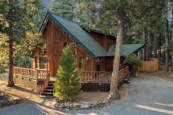 Een houten chalet met een groen dak, omringd door bomen, en een kleine trap naar de ingang.