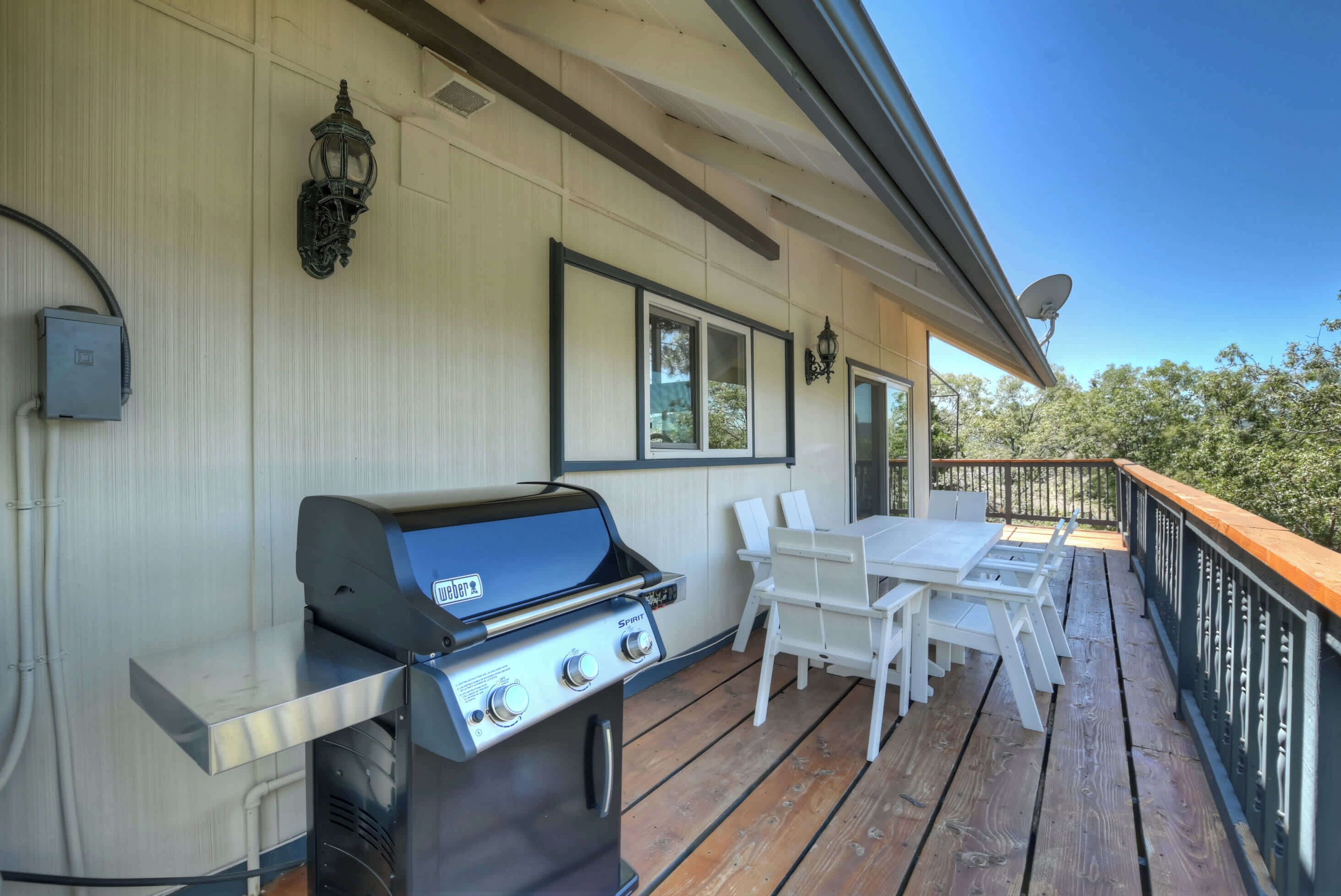 Une terrasse extérieure couverte, équipée d’un barbecue, de chaises blanches et d’une table.