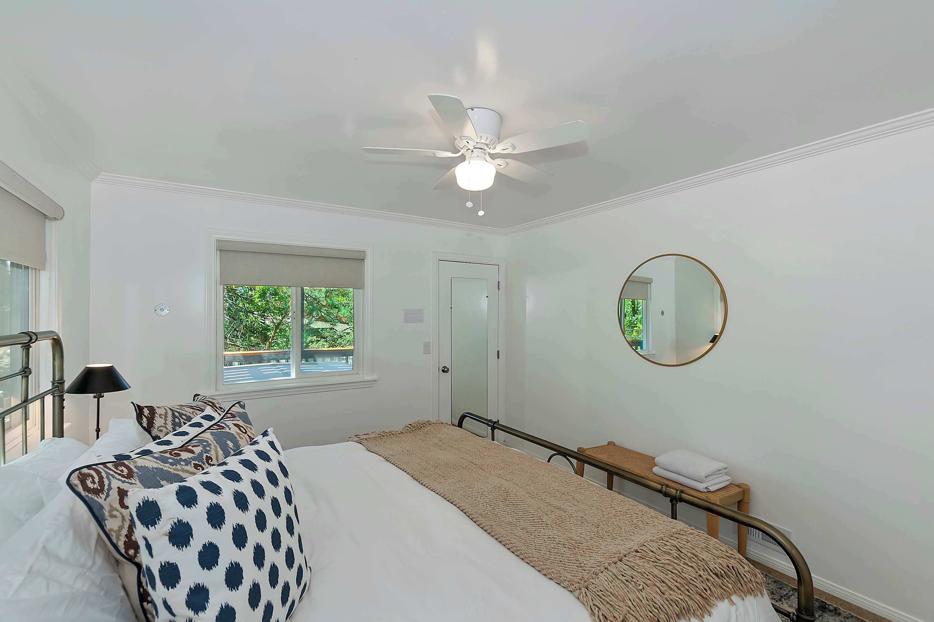 Ein Schlafzimmer mit Bett, Deckenventilator, Fenster, Nachttisch und Spiegel.