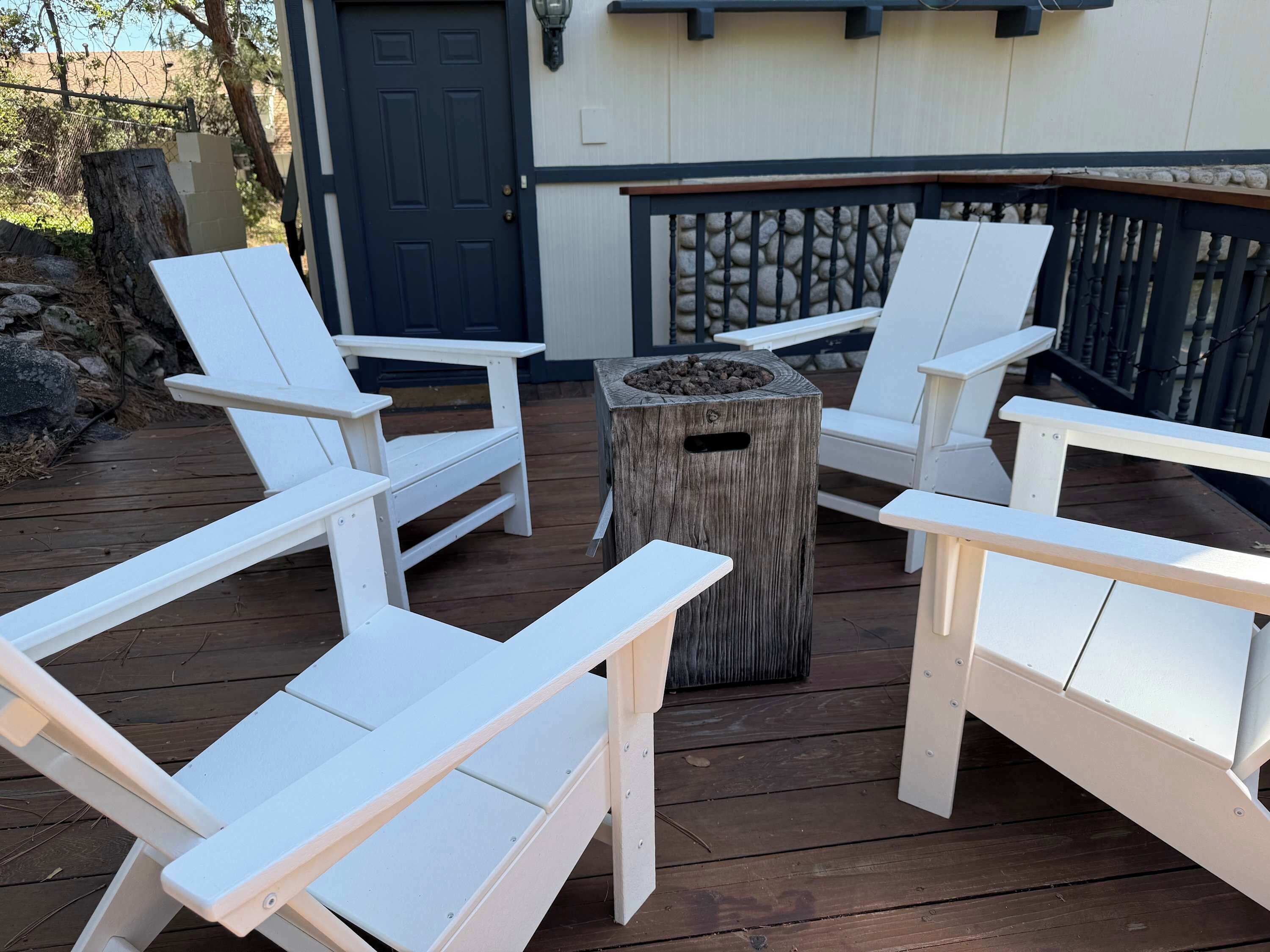 Una terraza con sillones Adirondack blancos dispuestos alrededor de una mesa de madera central.