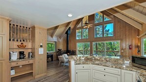 A spacious kitchen with wooden cabinets, granite countertops, and large windows offering views of the outdoors. - Casa Del Lago Spacious 4 Story Gated Home (Lake Arrowhead)