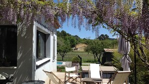 Eine Terrasse mit Gartenmöbeln, einem Grill und Blick auf ein Haus und ein Schwimmbecken.