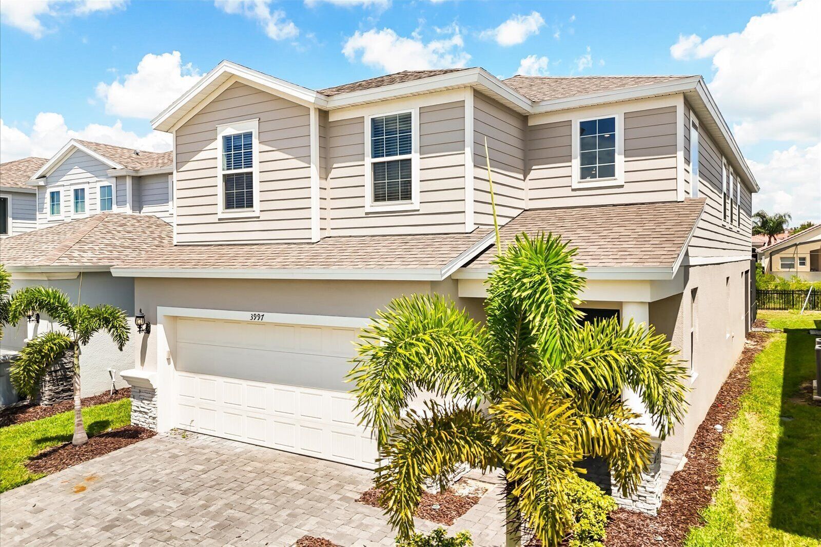 A two-story house with a garage, a well-maintained lawn, and a variety of plants.