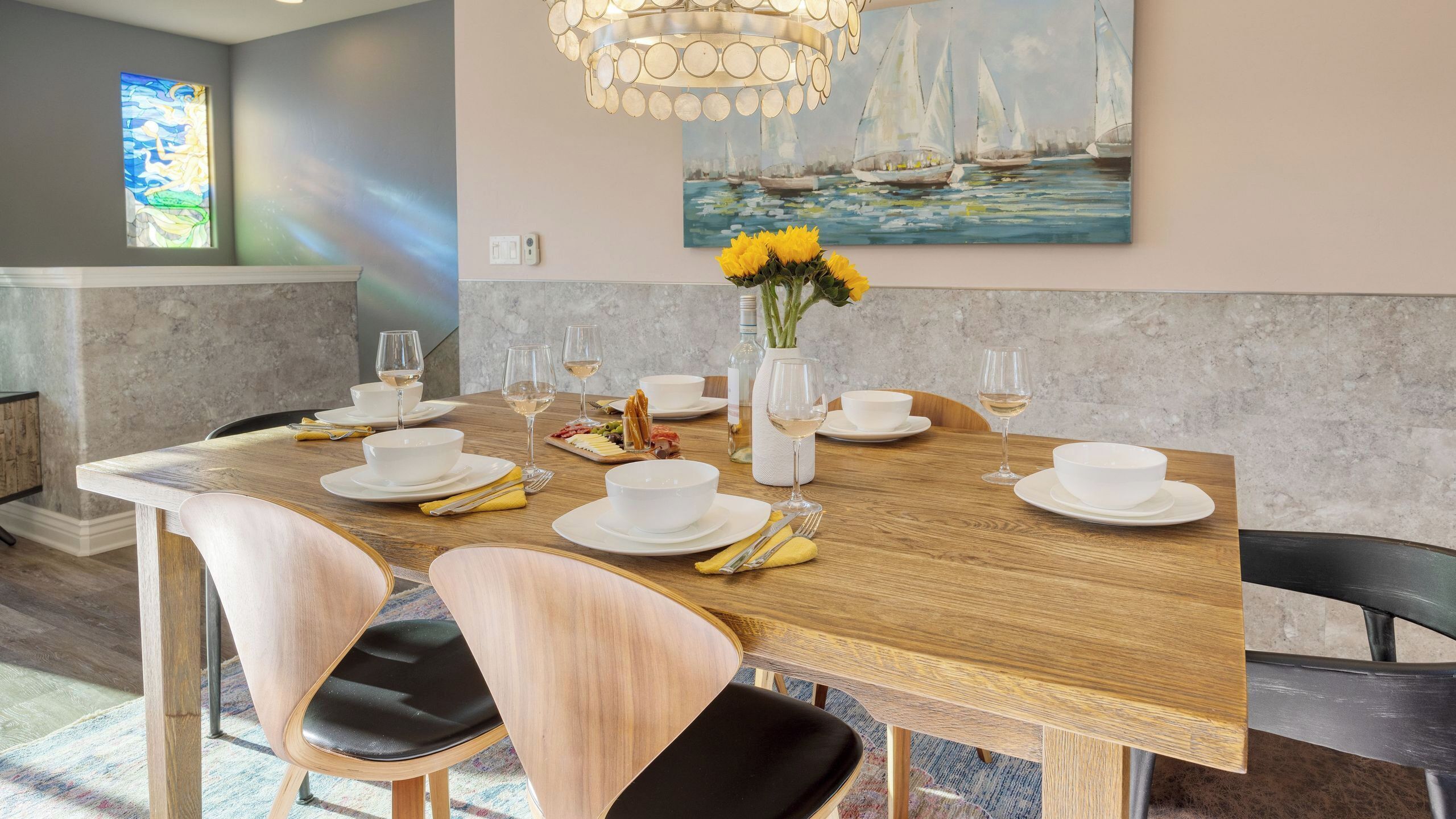 Een eetruimte met een houten tafel voor zes personen, witte borden en een vaas met gele bloemen.