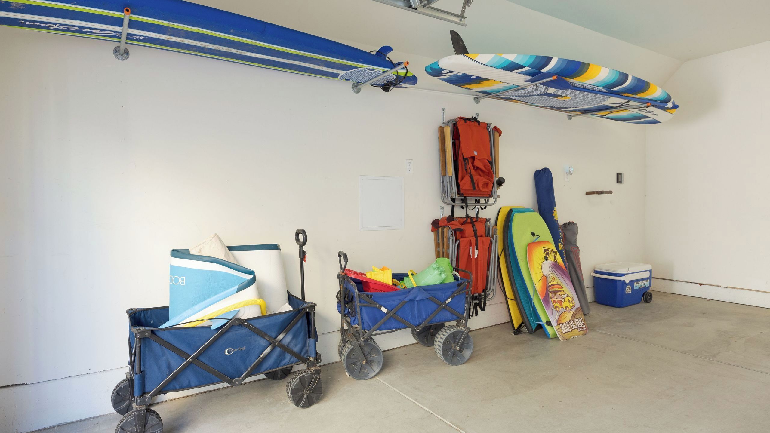 A storage room with a cart, a stroller, a surfboard, and a cooler.