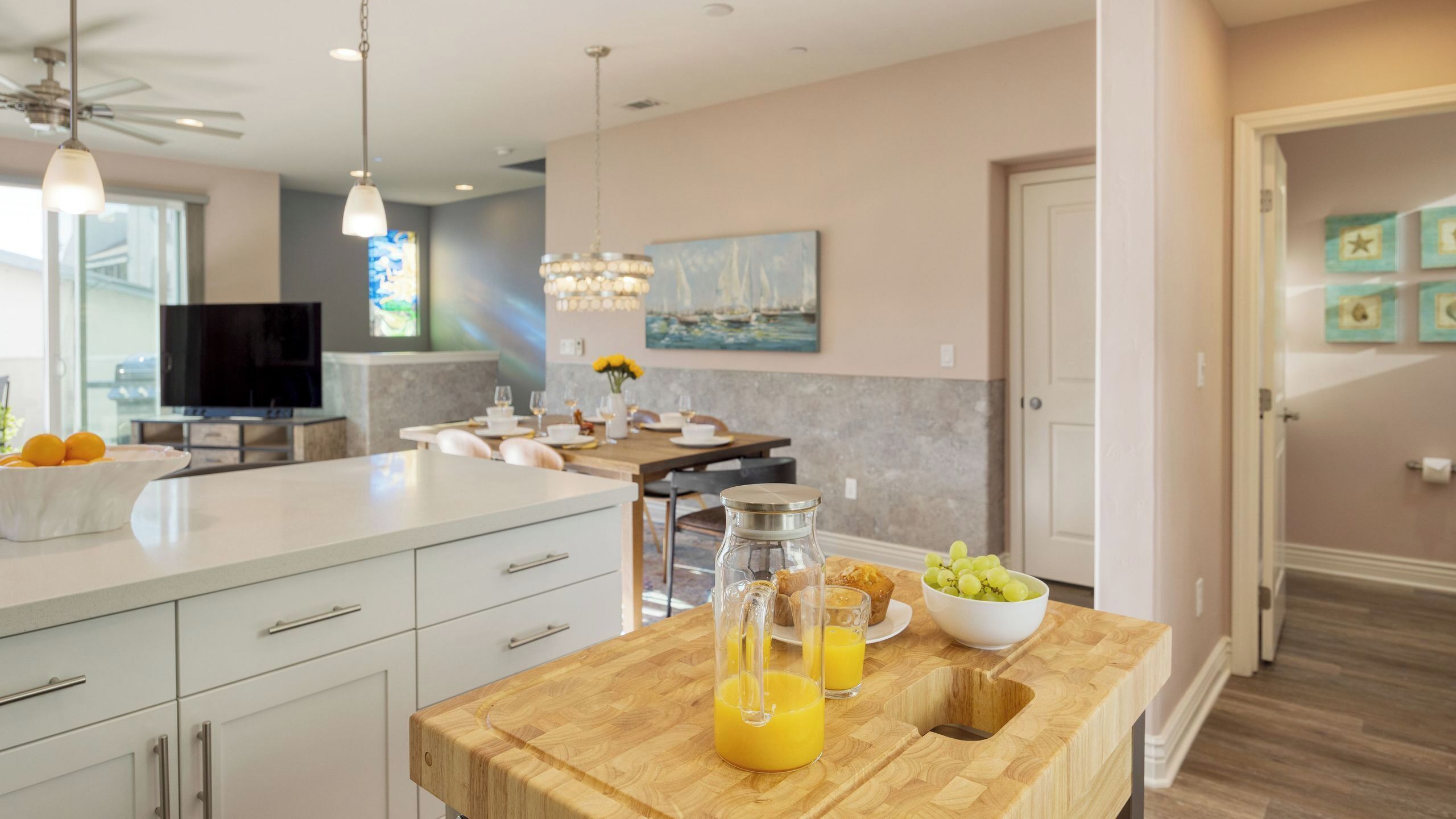 A modern kitchen with a wooden island, a dining area, and a living space with a TV and artwork.