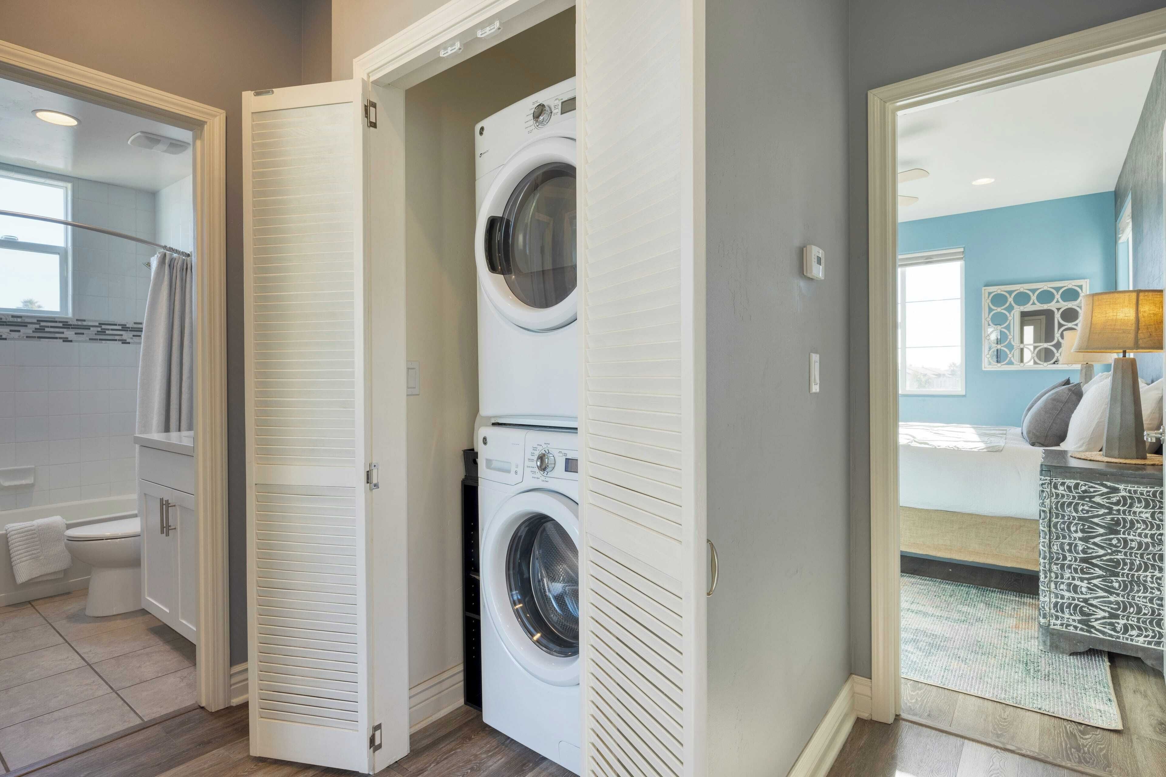 Une buanderie équipée d’un lave-linge et d’un sèche-linge à chargement frontal, d’un meuble blanc et d’une porte donnant sur une autre pièce.