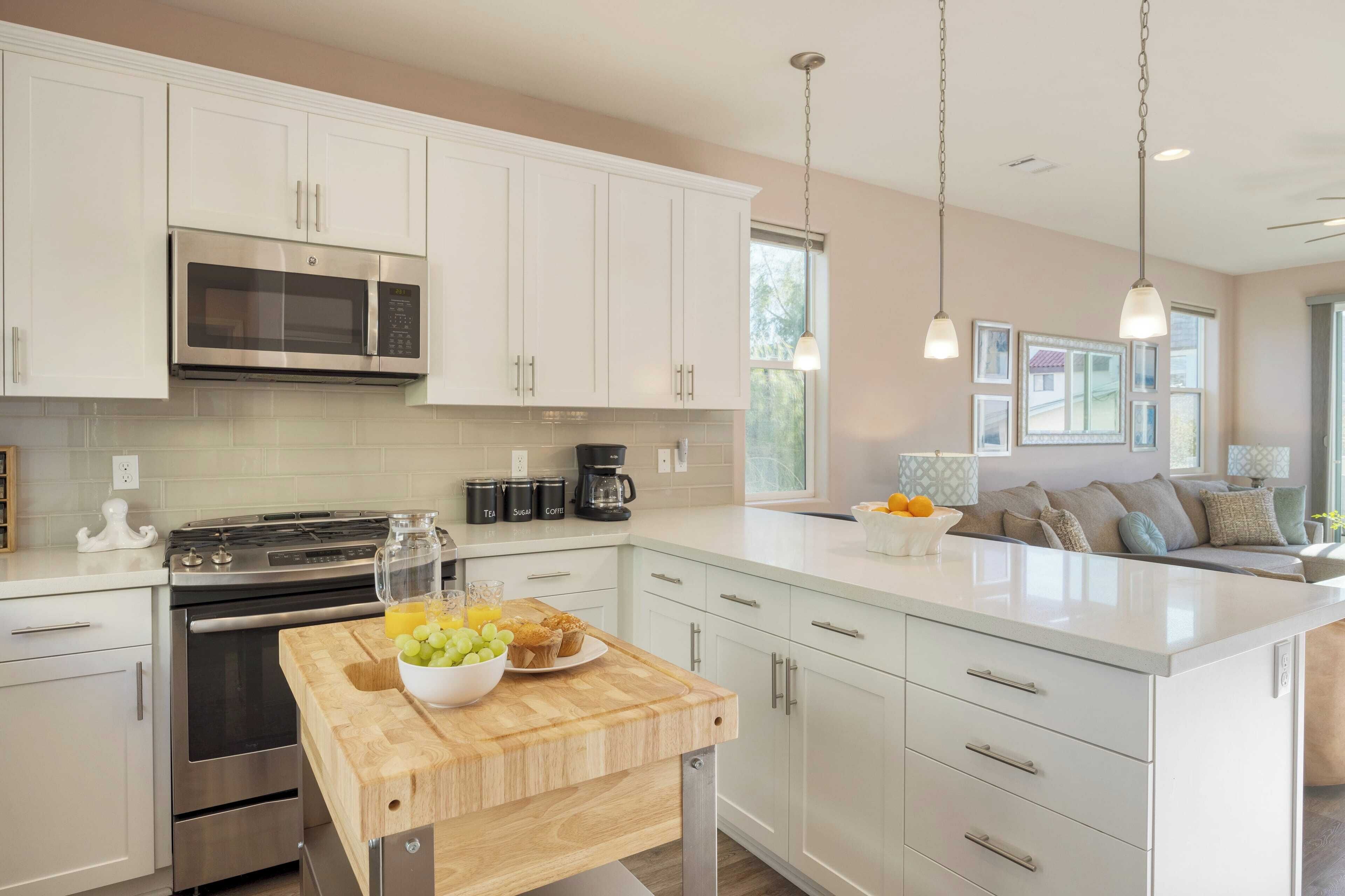 A modern kitchen with white cabinetry, stainless steel appliances, and a central island with a cutting board and fruit bowl.