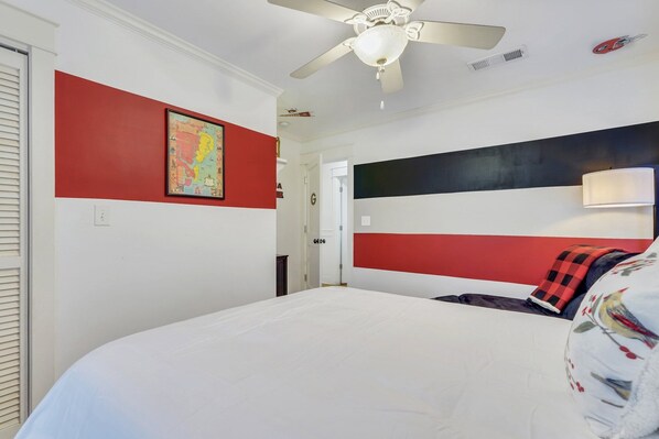 A bedroom with a large bed, a ceiling fan, a red and black headboard, and a colorful map on the wall.
